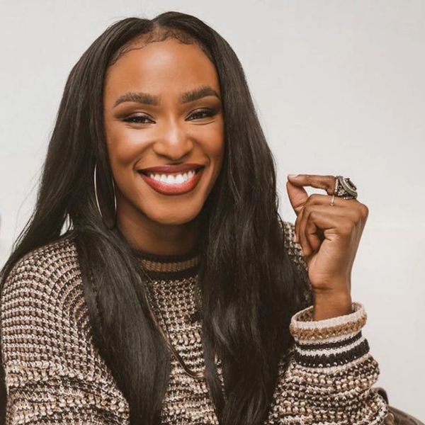 A woman with long hair smiles brightly, wearing a patterned top and rings.