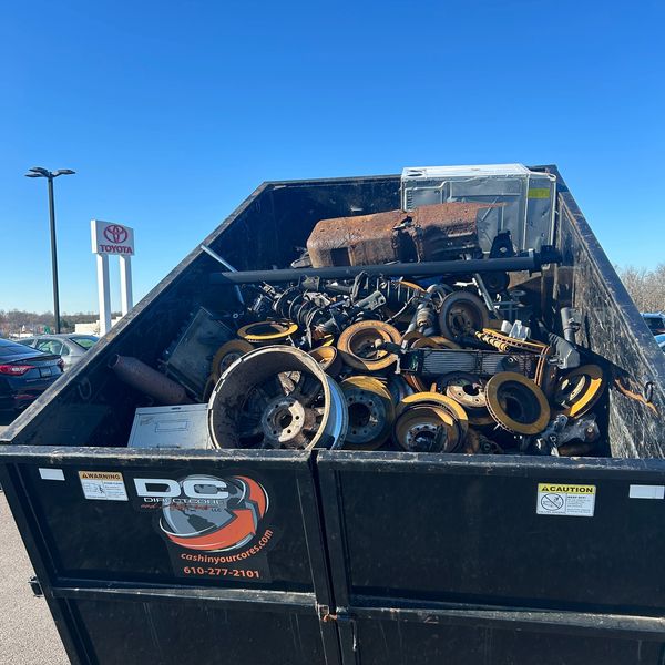 A large black dumpster filled with rusty metal parts under a clear blue sky.