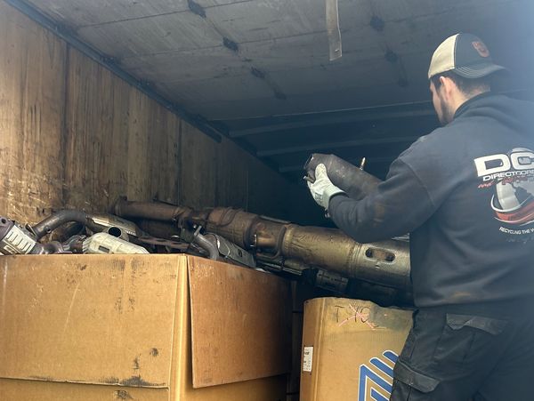 Worker unloading car exhaust parts from a truck onto pallets.