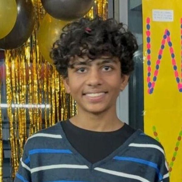A smiling young person with curly hair stands in front of festive gold and black decorations.