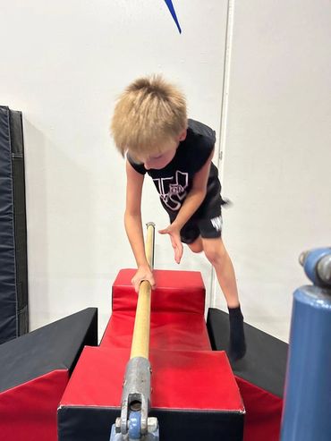 A young boy jumping over a bar, with one hand on the bar.