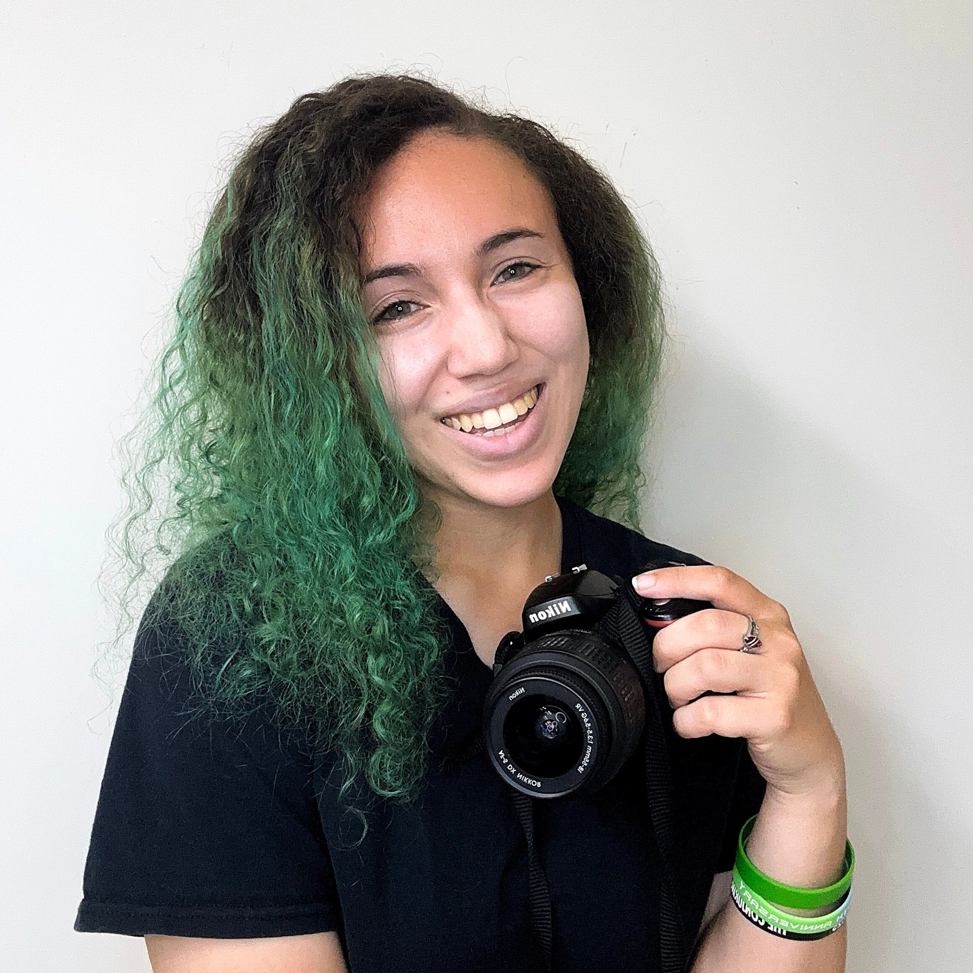 Smiling person with green hair holding a Nikon camera.