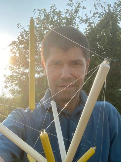 Steve Thomas Looking at the Camera Outside from Behind a Tensegrity Model