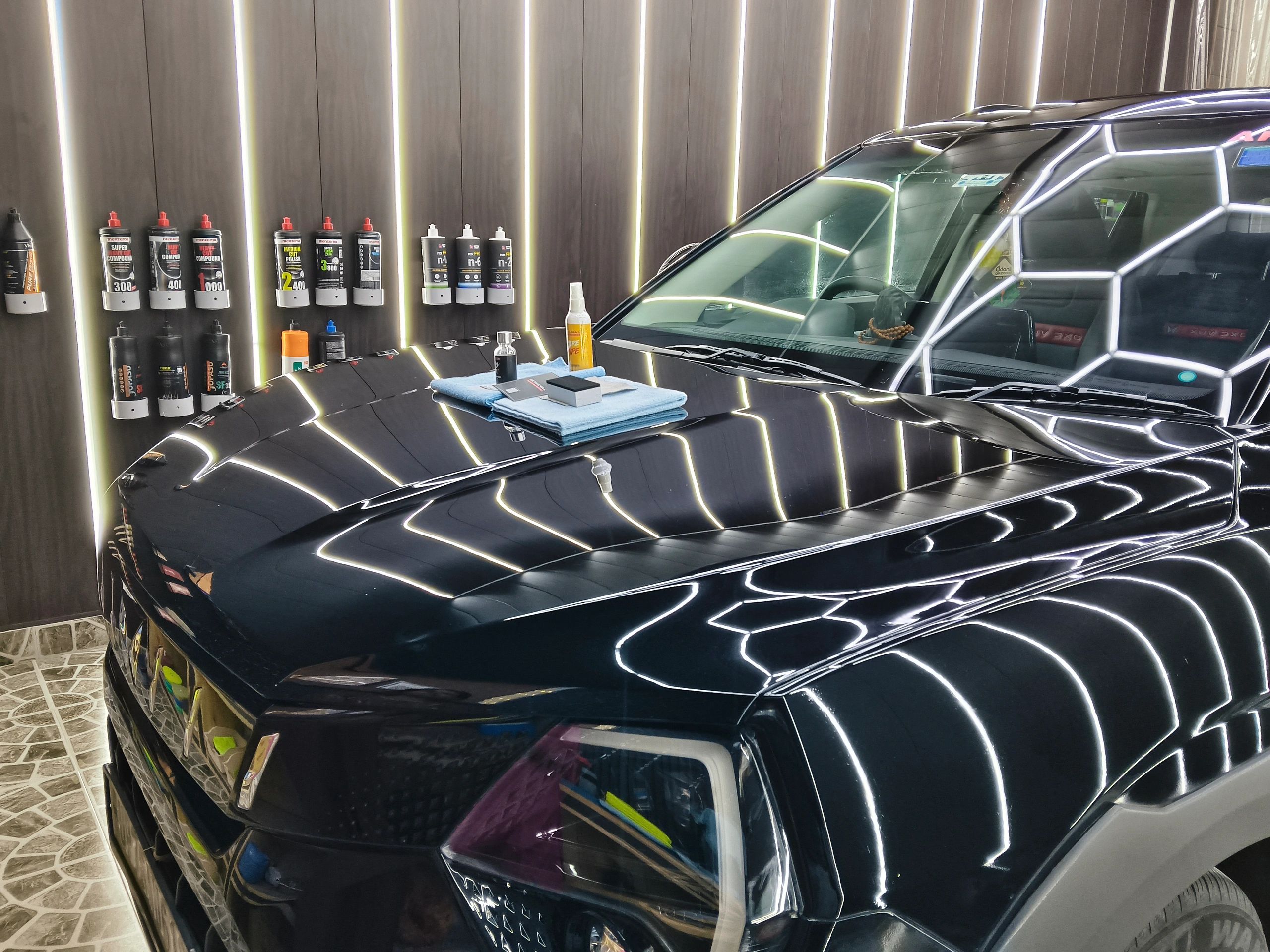 Black car with detailing products on the wall and hood.