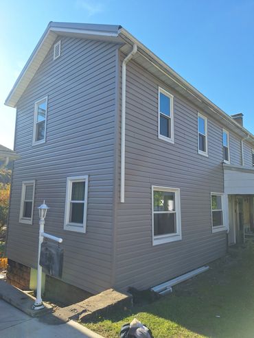 Two-story house with gray siding and multiple windows under a clear blue sky.