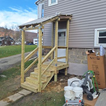 Newly constructed wooden porch with stairs and roof attached to a house.