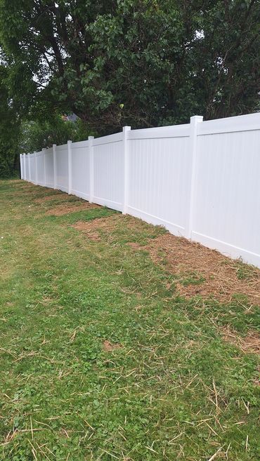 A long white vinyl fence runs alongside a grassy yard with trees in the background.