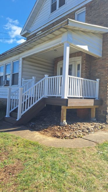 Newly constructed porch with white railings and wooden stairs on a sunny day.
