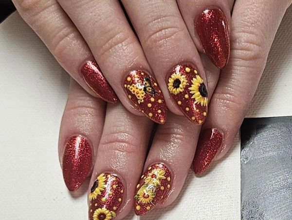 Red glitter nails with sunflower designs.