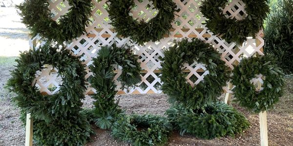 Christmas wreaths displayed on a white lattice under a red and white tent.