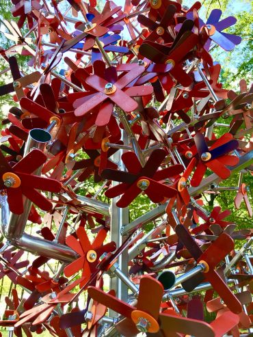 Close-up of a red metal flower sculpture with green trees in the background.