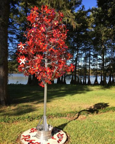 Metal sculpture resembling a tree with red flowers in a park.