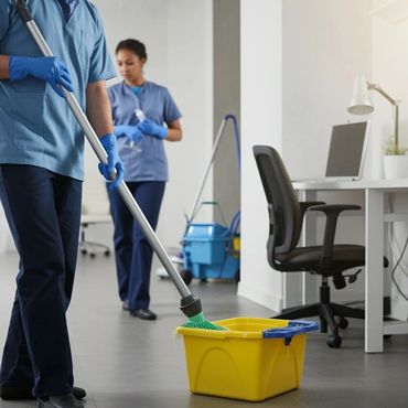 Two janitors cleaning an office space with a mop and spray bottle.