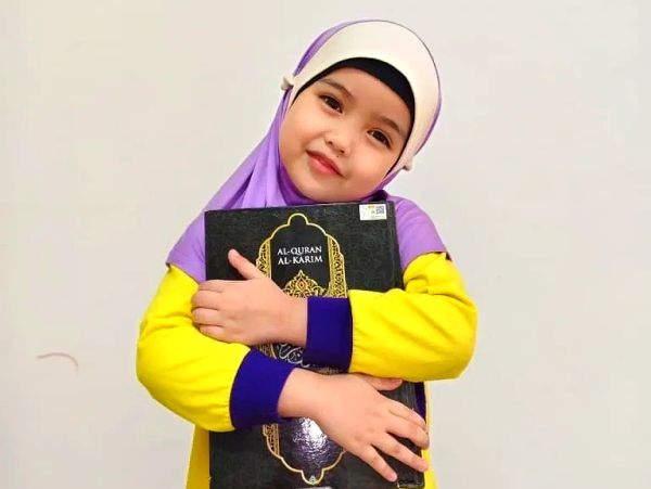 Young girl in hijab hugging the Quran.