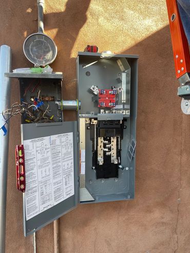 Open electrical meter and panel on a wall with tools nearby.