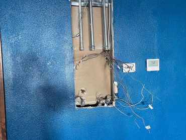 Exposed electrical wiring and conduits on a blue wall.