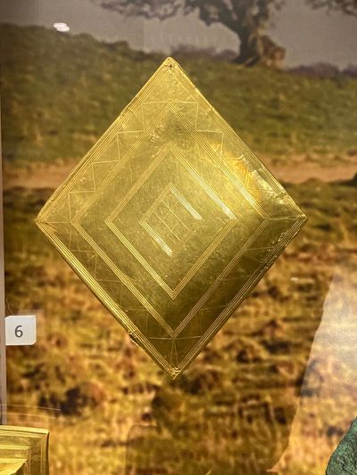 A gold diamond shape object with intricate markings.