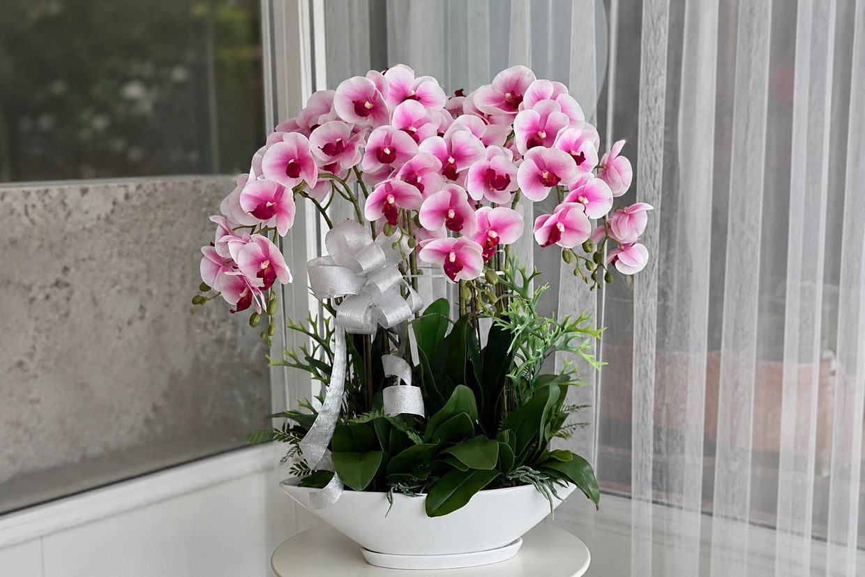 Elegant pink orchids in a white vase with a silver ribbon.