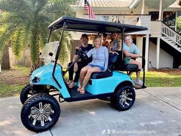 Four people sitting on a blue golf cart outside a house with palm trees.