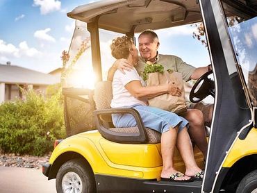 Elderly couple sharing a tender moment in a yellow golf cart with groceries.
