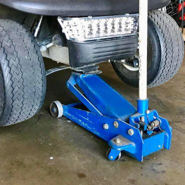 Blue hydraulic floor jack lifting a vehicle with large tires.