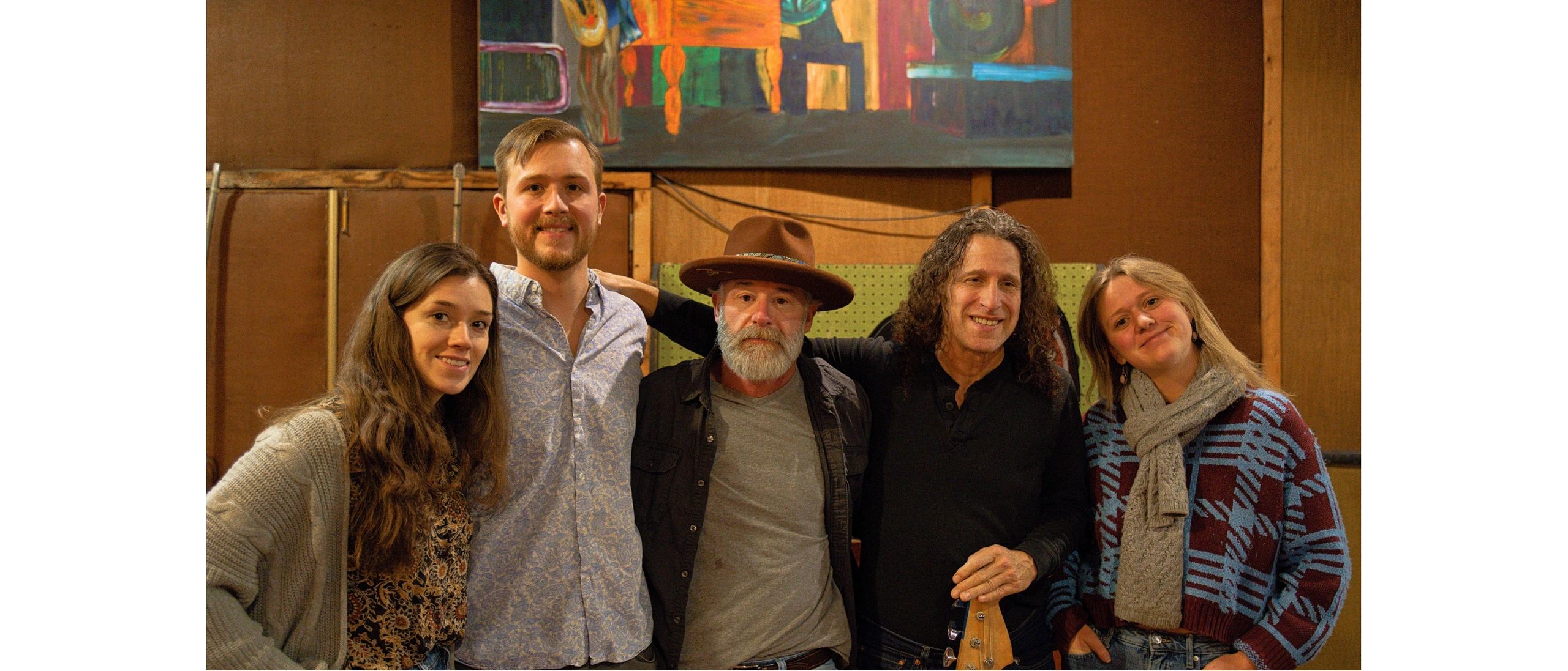 Five people posing together in a cozy indoor setting with warm lighting.