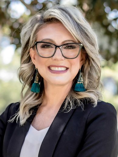 Smiling woman with glasses and teal earrings outdoors.