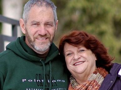 Smiling middle-aged couple posing outdoors in casual attire.