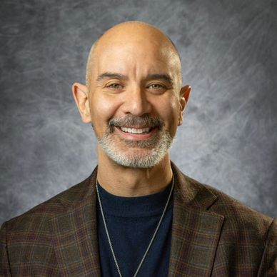 Smiling bald man with a beard wearing a plaid blazer and black shirt.