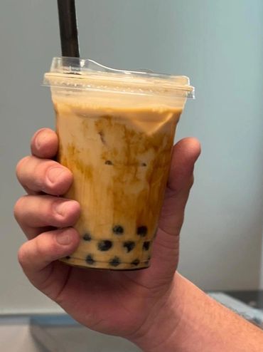 Hand holding a cup of brown sugar bubble tea with black tapioca pearls.