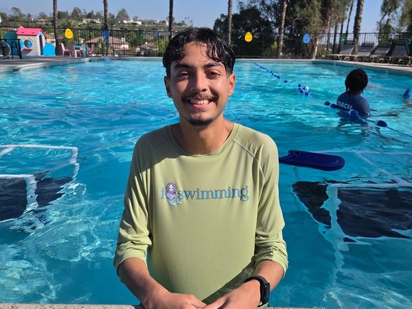 Smiling young man in a swimming shirt at the edge of a pool on a sunny day.