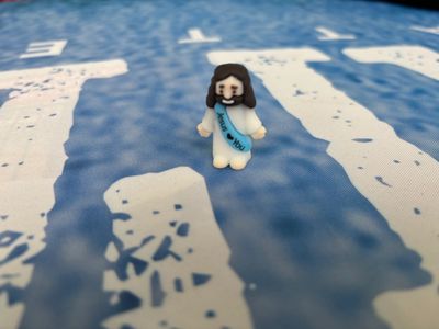 A small figurine of Jesus with a sash saying 'Jesus loves you' on a blue and white textured surface.