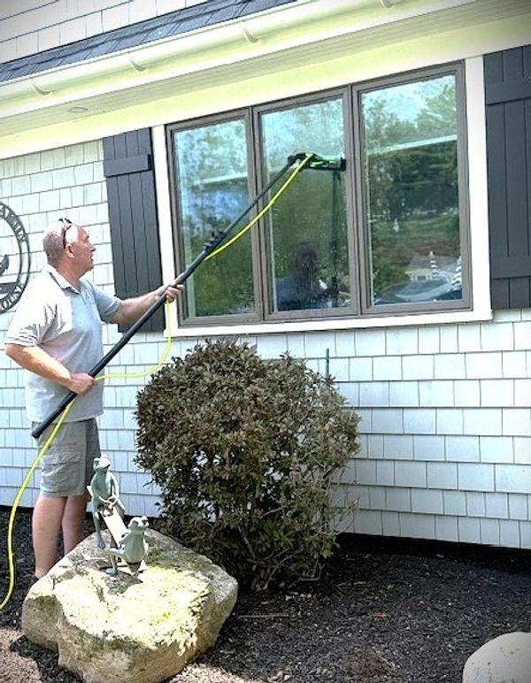 Man cleaning house windows with a long pole brush.