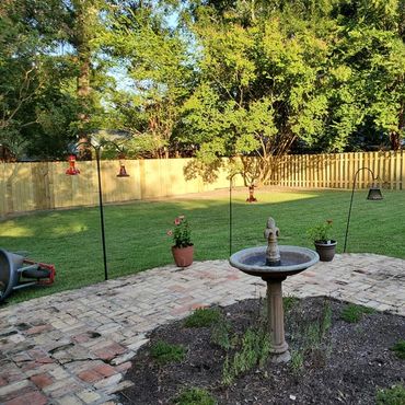 Wood privacy fence surrounding a landscaped backyard with a brick patio and garden area.