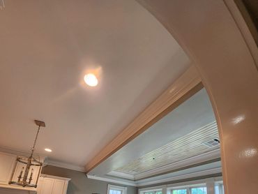 “Living room with a coffered ceiling, crown molding, arched openings, and a fireplace.”