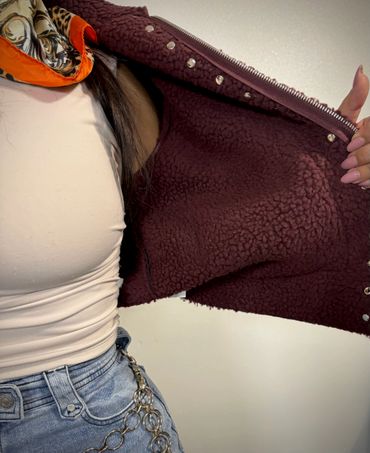 Person wearing a beige top, light blue jeans, and a maroon fleece jacket.