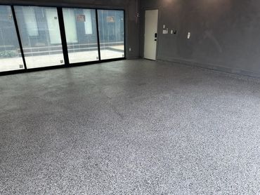 Empty room with speckled gray flooring and large windows.