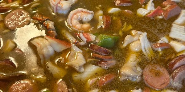 A close-up of a seafood gumbo with shrimp, sausage, and crab in broth.