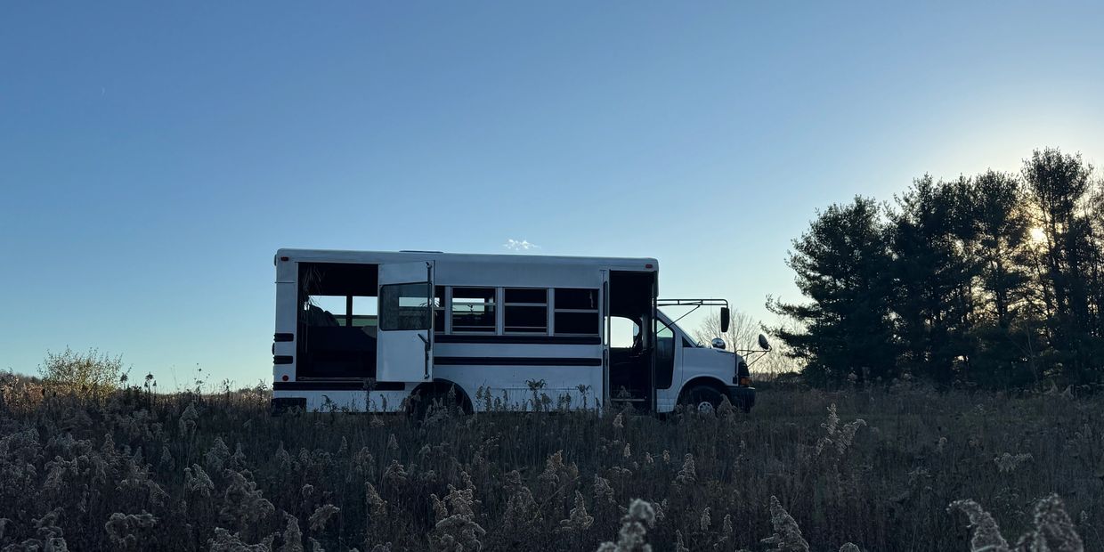 White bus with open doors in a field at sunset.