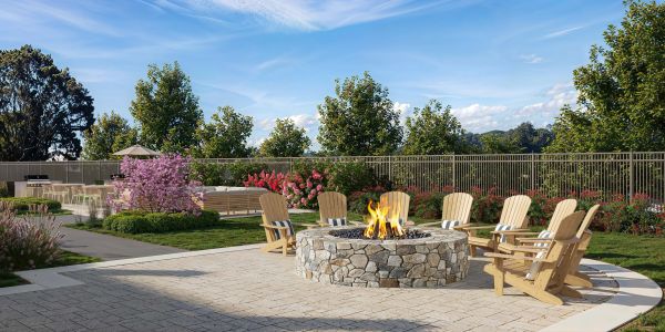 Outdoor fire pit with wooden chairs in a landscaped garden under clear blue sky.