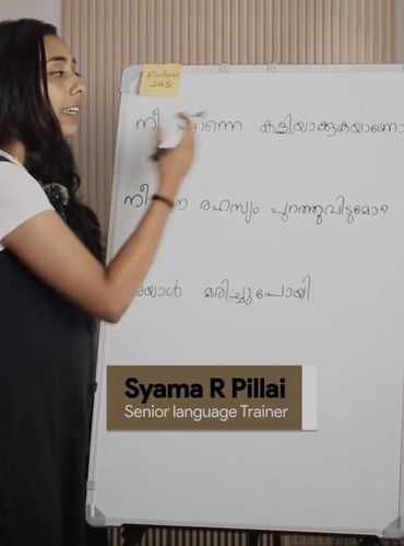 A language trainer named Syama R Pillai teaching with a whiteboard in Malayalam.