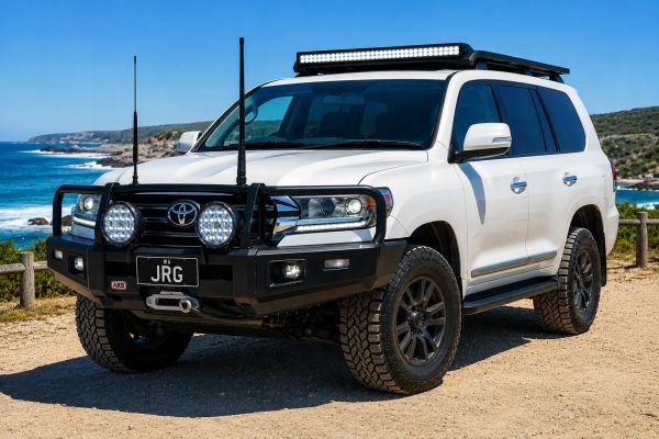 White Toyota Land Cruiser with off-road modifications on a dirt path by the coast.