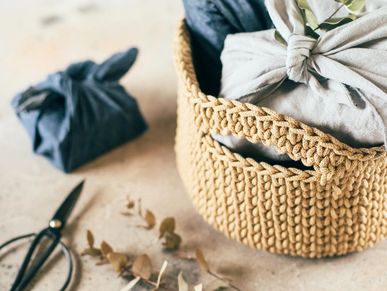A woven basket holding fabric-wrapped items with scissors and dried leaves nearby.