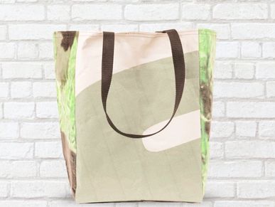 Reusable grocery bag with brown handles against a white brick wall.
