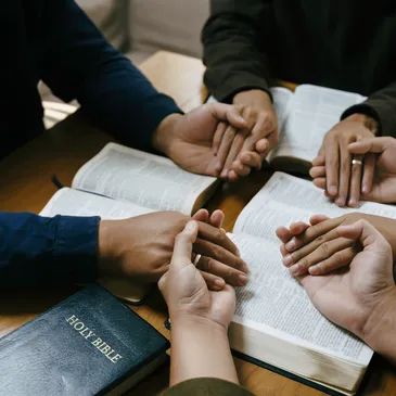 People holding hands in prayer over open Bibles.