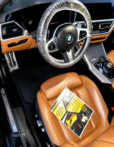 BMW car interior with plastic-covered steering wheel and brown leather seats.