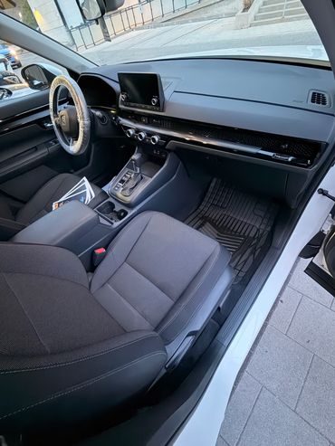 Interior view of a modern car with touchscreen and plastic-wrapped steering wheel.