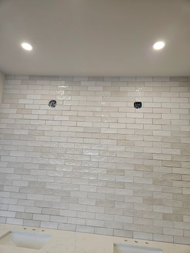 White tiled bathroom wall with two recessed lights and two sink cutouts.