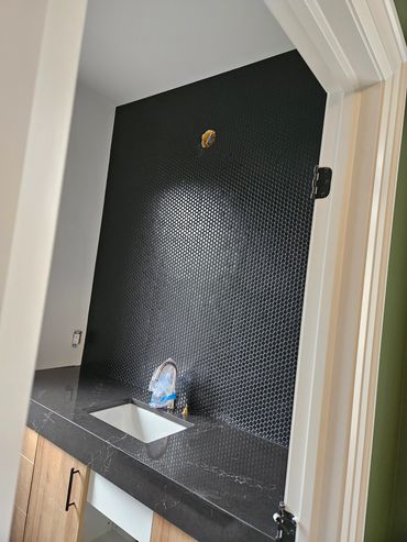 Modern bathroom with black penny tile backsplash and sleek countertop.