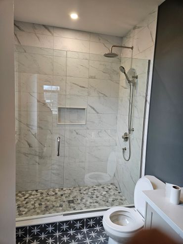 Modern bathroom with glass shower, pebble floor, and patterned tile.